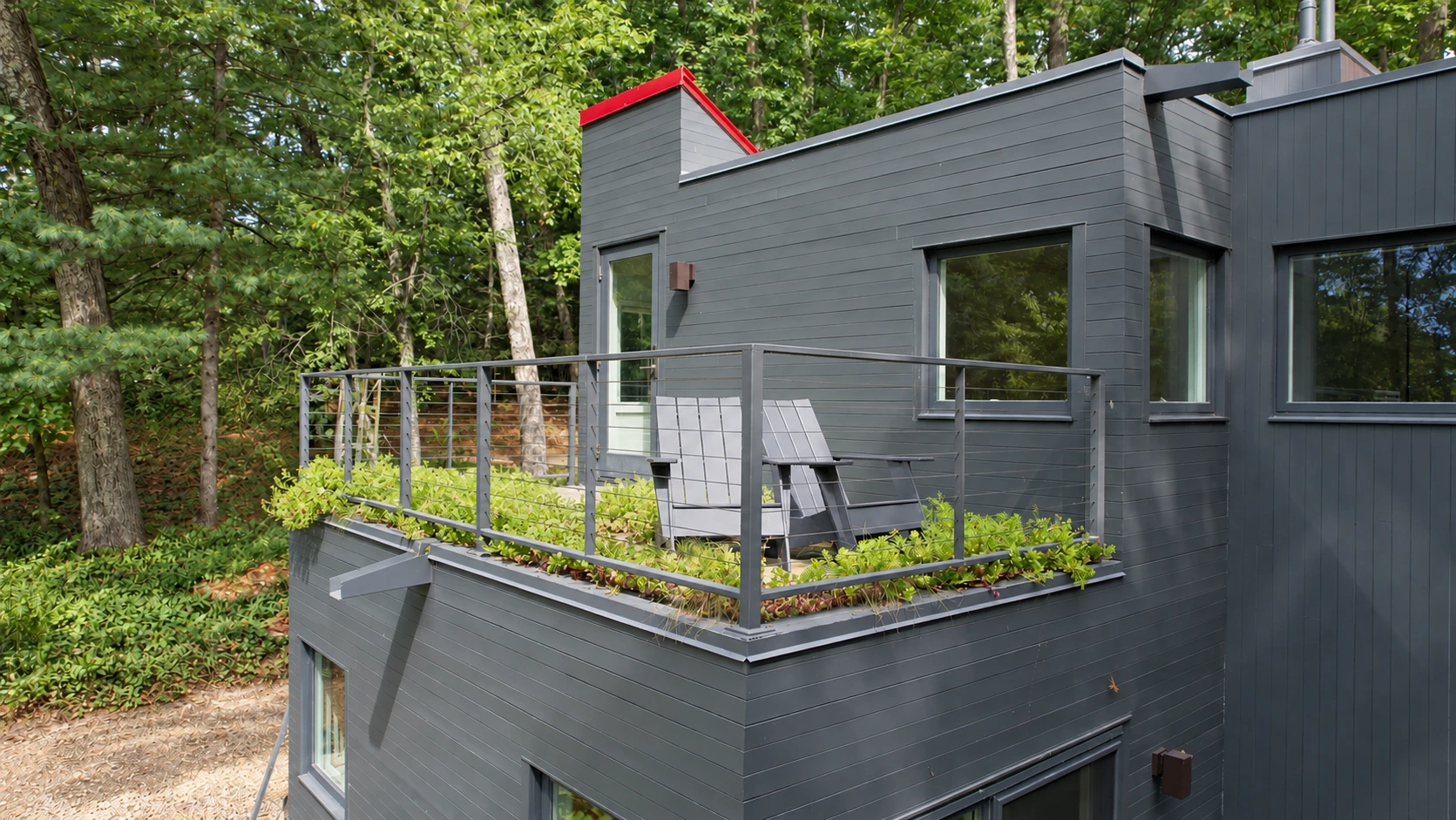 Planted roof and seating area beside a dark-clad house in a wooded landscape