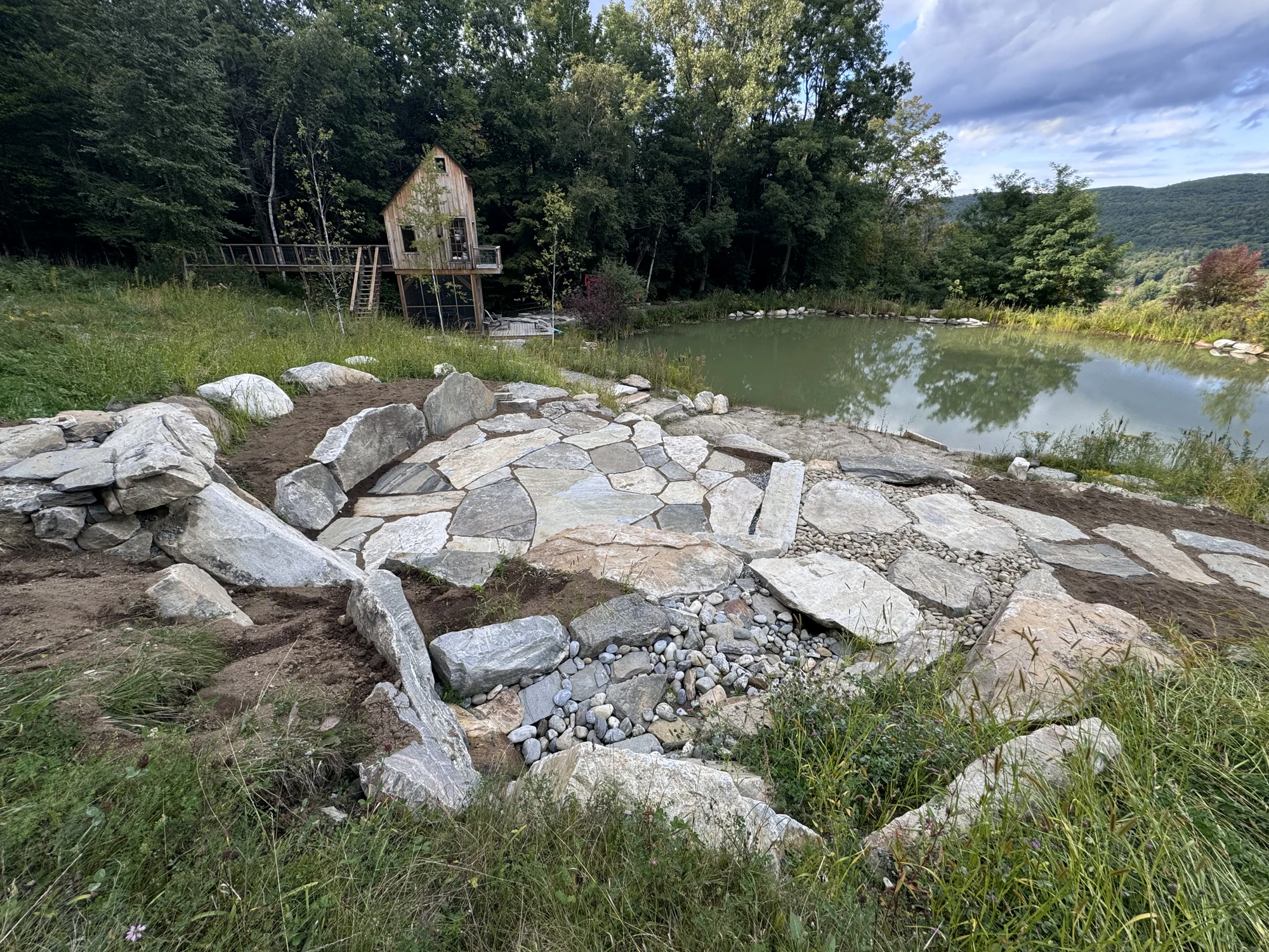 Fitted natural stone paving, boulder edges, and drainage details beside the pond