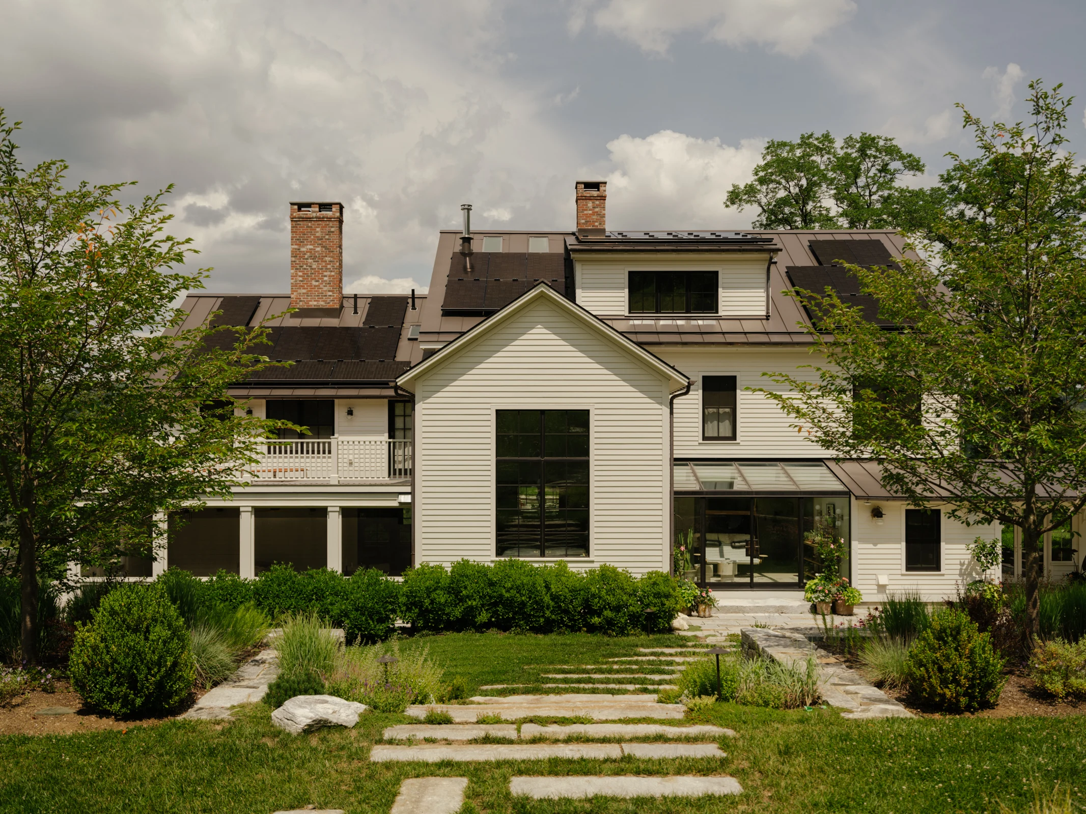 Viewed from the pool terrace, the house is framed by surrounding trees, shrubs, and garden planting. Broad stone steps draw the eye toward the house, connecting the terrace with the garden and architecture.